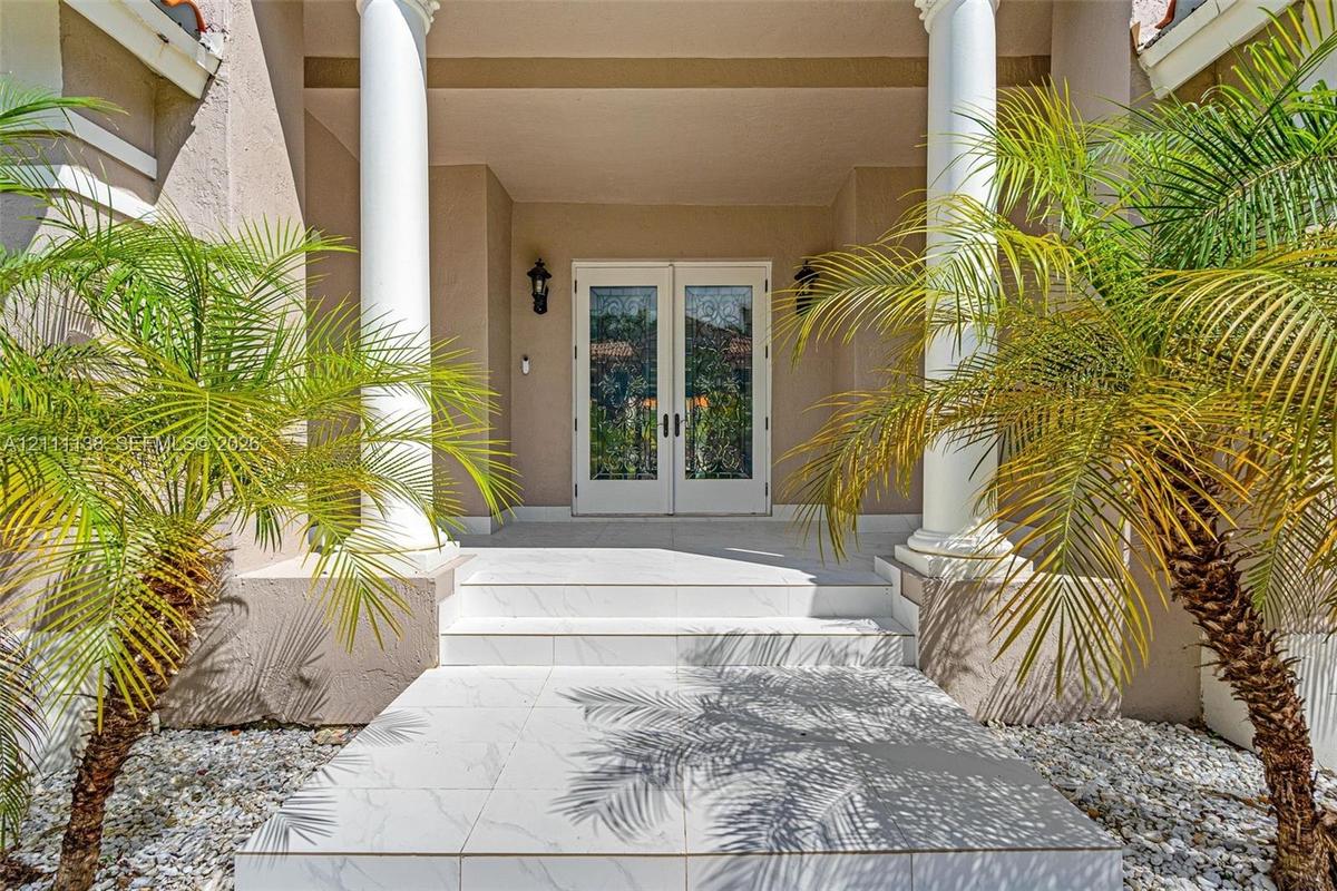 Covered entryway featuring dual white columns, stone-tile steps, glass-paned double entry doors, and wall-mounted exterior lanterns