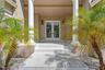 Covered entryway featuring dual white columns, stone-tile steps, glass-paned double entry doors, and wall-mounted exterior lanterns