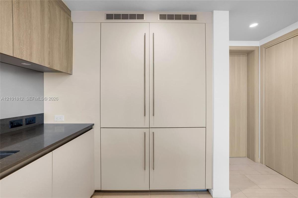 Built-in floor-to-ceiling cabinetry with matte finish, light wood-finish upper cabinets, dark solid surface countertop, and integrated panel-ready app
