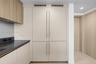 Built-in floor-to-ceiling cabinetry with matte finish, light wood-finish upper cabinets, dark solid surface countertop, and integrated panel-ready app
