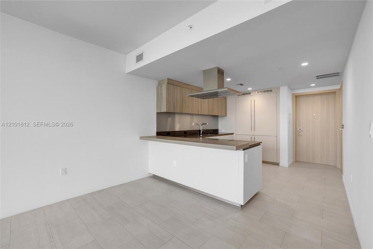 Kitchen featuring wood-finish upper cabinetry, a stainless steel range hood, integrated refrigerator, stone-surface countertop, and ceramic tile floor