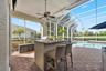Covered lanai featuring a stone-topped outdoor kitchen, built-in grill, ceiling fan, and decorative paver flooring, fully enclosed by a screened pool 