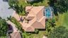 Aerial view featuring a tile roof, screened-in swimming pool with spa, paver driveway, and mature landscaping