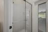 Shower enclosure featuring a chrome-framed sliding glass door, white tiled walls, and an exterior door with integrated blinds