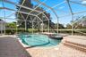 Screen-enclosed pool area featuring a spillover spa, tiled deck, and brick-style pavers