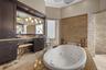 Bathroom featuring a deep soaking tub with a stone-surround deck, stacked stone wall accents, dark wood-finish cabinetry, and a large framed mirror wi