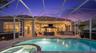 Screened lanai featuring a paver patio, integrated swimming pool with spa, and outdoor bar