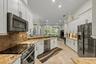 Kitchen featuring white cabinetry with dark hardware, stone-finish countertops, brick-style tile backsplash, stainless steel appliances, and tile floo