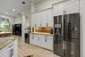 Kitchen featuring white cabinetry with matte black hardware, stone-finish countertops, tiled backsplash, stainless steel refrigerator, and stone-finis