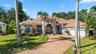 Stucco exterior featuring a clay tile roof, arched windows, grand recessed entryway, and a paver driveway leading to an attached three-car garage