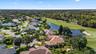 Aerial perspective featuring a multi-hipped roof residence positioned alongside a golf course fairway and a water feature, incorporating mature trees 