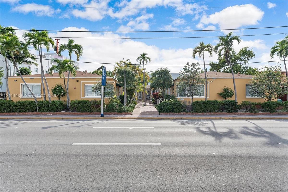 Low-rise exterior featuring a stucco facade, horizontal-sliding windows, mature palm trees, and landscaped shrubbery
