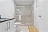 Bathroom featuring a walk-in shower with floor-to-ceiling neutral tile surround, sliding glass enclosure, white vanity cabinet with a contrasting coun