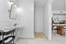 Wall-mounted vitreous china sink with a single-handle chrome faucet, rectangular tilt mirror, overhead vanity lighting, and light-toned tile flooring