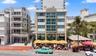 Multi-story building exterior featuring Art Deco architectural details, glass-paneled balconies, floor-to-ceiling windows, and a ground-level covered 