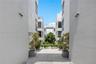 Modern multi-story exterior featuring smooth stucco siding, large windows, an overhead structural walkway, and central courtyard landscaping with ston