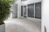 Covered entryway featuring large-format concrete flooring, floor-to-ceiling glass paneling, a full-lite glass entry door, and white stucco walls