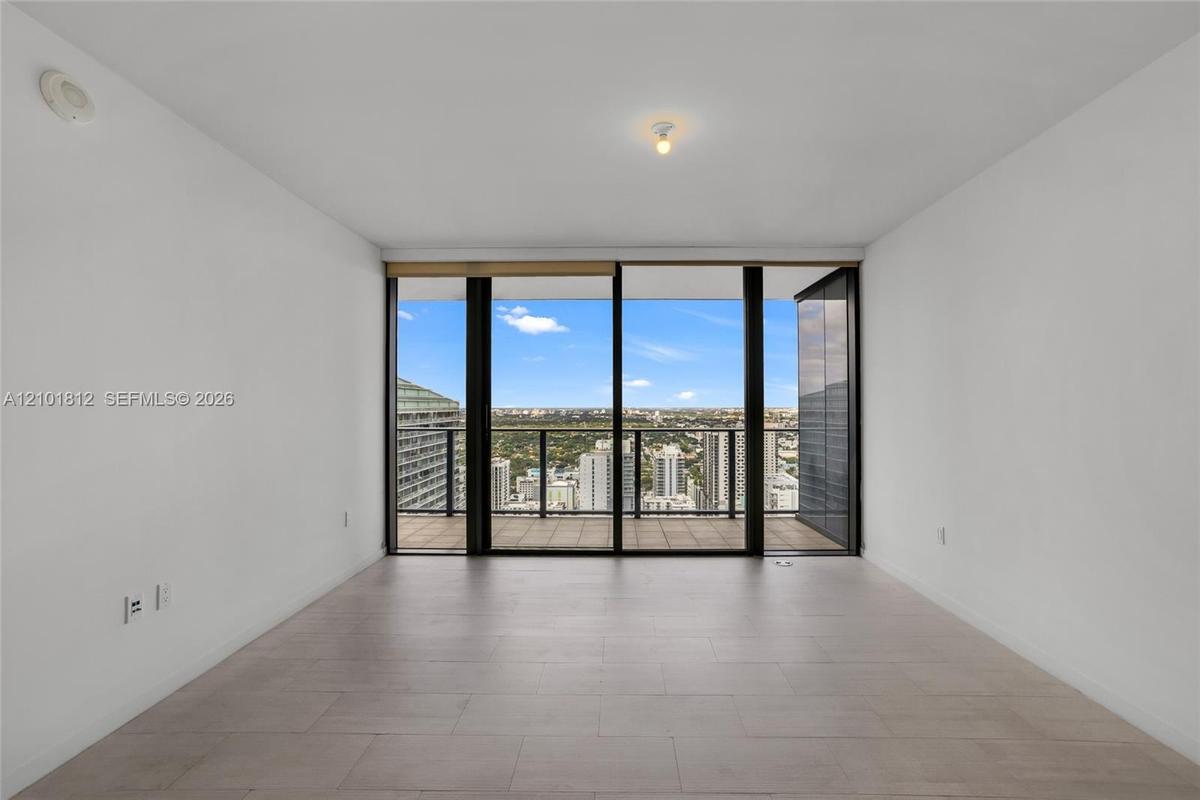 Floor-to-ceiling sliding glass doors, private balcony with metal railing, and neutral tile flooring