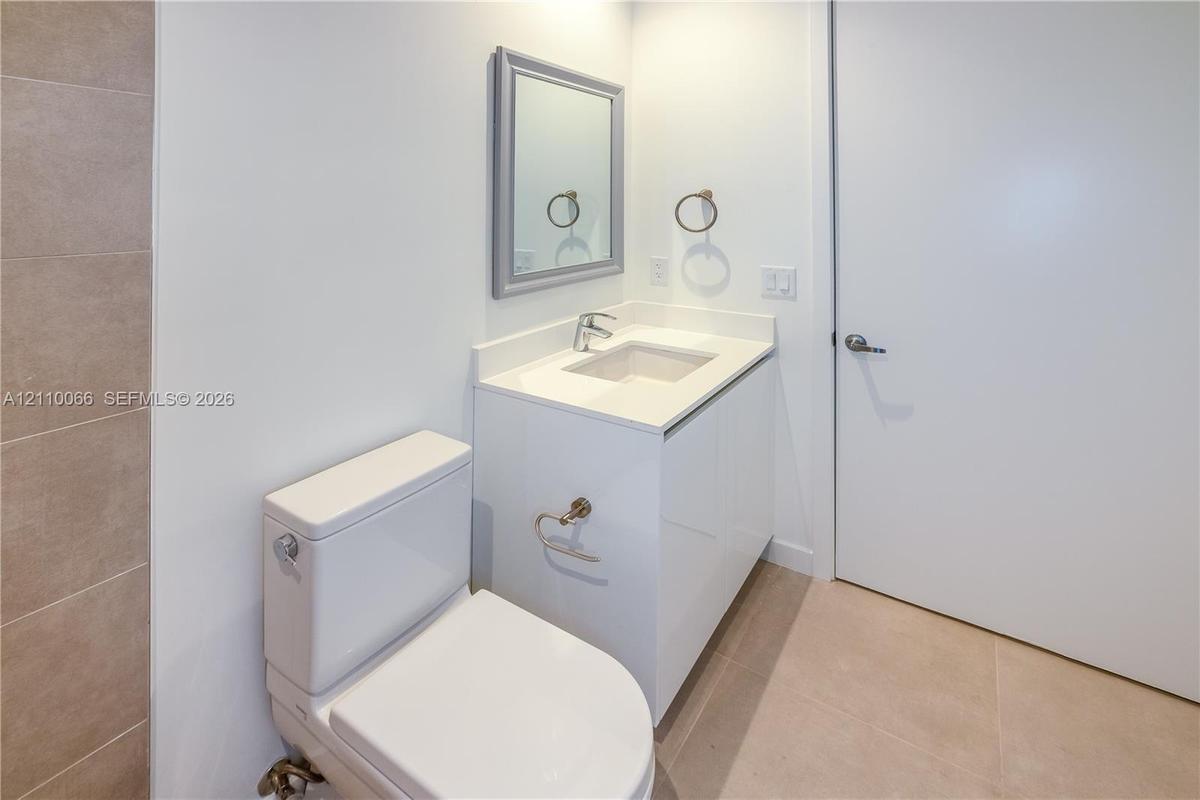 Modern vanity featuring a white cabinet base, clean-lined countertop with an integrated rectangular sink, wall-mounted mirror, and ceramic tile floori
