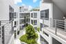 Modern multi-story structure featuring a smooth white stucco facade, tiered metal railings, expansive glass windows, and an open-air central courtyard