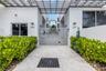 Modern exterior featuring smooth-stucco facade, horizontal slatted metal security gate, overhead metal trellis, and integrated wall-mounted lighting