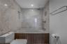 Full-height stone wall tiling, built-in soaking tub with wood-finish paneling, recessed shower niche, ceiling-mounted rainfall showerhead, and wall-mo