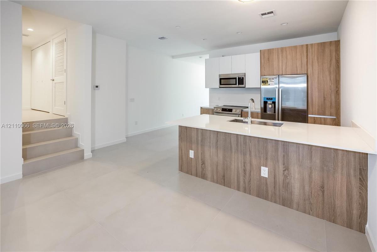 Kitchen featuring dual-tone cabinetry with wood-finish and matte white uppers, quartz countertops, a central island, stainless steel appliances, and l