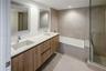 Floating dual-sink vanity with wood-finish cabinetry, solid-surface countertop, separate glass-enclosed shower, and deep soaking tub with neutral tile