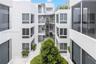 Modern multi-level exterior architecture featuring smooth stucco facades, expansive floor-to-ceiling windows, open-air walkways, metal railings, and i