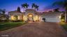 Stucco exterior featuring a tiled roof, arched entryway, paved driveway, and established palm trees