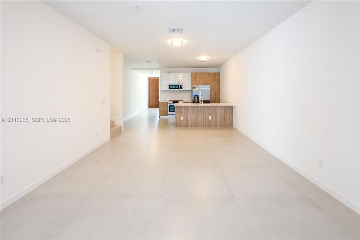Kitchen featuring white high-gloss upper cabinetry, wood-finish base cabinetry, stainless steel appliances, and a central island with a countertop