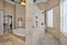Bathroom featuring a jetted soaking tub with a stone-finished deck, walk-in shower with natural stone tile walls, pebble floor inlay, and recessed wal