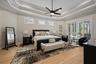 Tray ceiling with crown molding, wood-finish flooring, central ceiling fan, multiple wall-mounted plantation shutters, and sliding glass doors