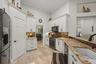 Kitchen featuring white cabinetry, stone countertops, a farmhouse-style sink, tiled backsplash, and stone-finish flooring
