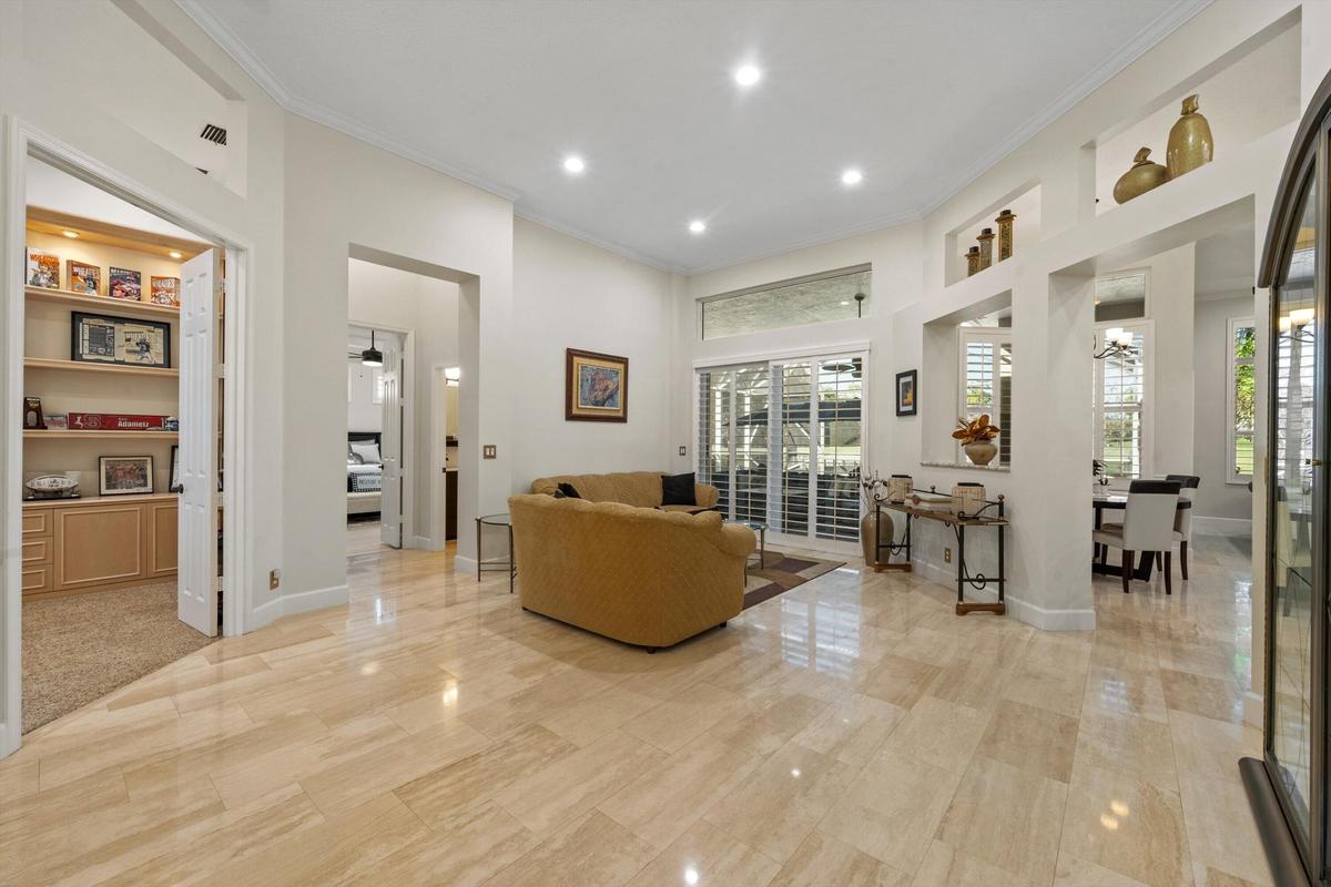 High-ceiling living area featuring large-format tile flooring, built-in recessed wall shelving, a transom window, and sliding glass doors