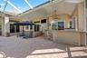 Covered lanai featuring a screen enclosure, paver flooring, built-in outdoor bar with stone countertop, and ceiling fans