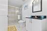 Bathroom featuring a white vanity cabinet with a dark stone countertop, an integrated sink, a framed mirror with integrated lighting, and a walk-in sh