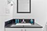 Vanity featuring a dark stone countertop, integrated rectangular sink, chrome faucet, wall-mounted mirror, and glass shelving