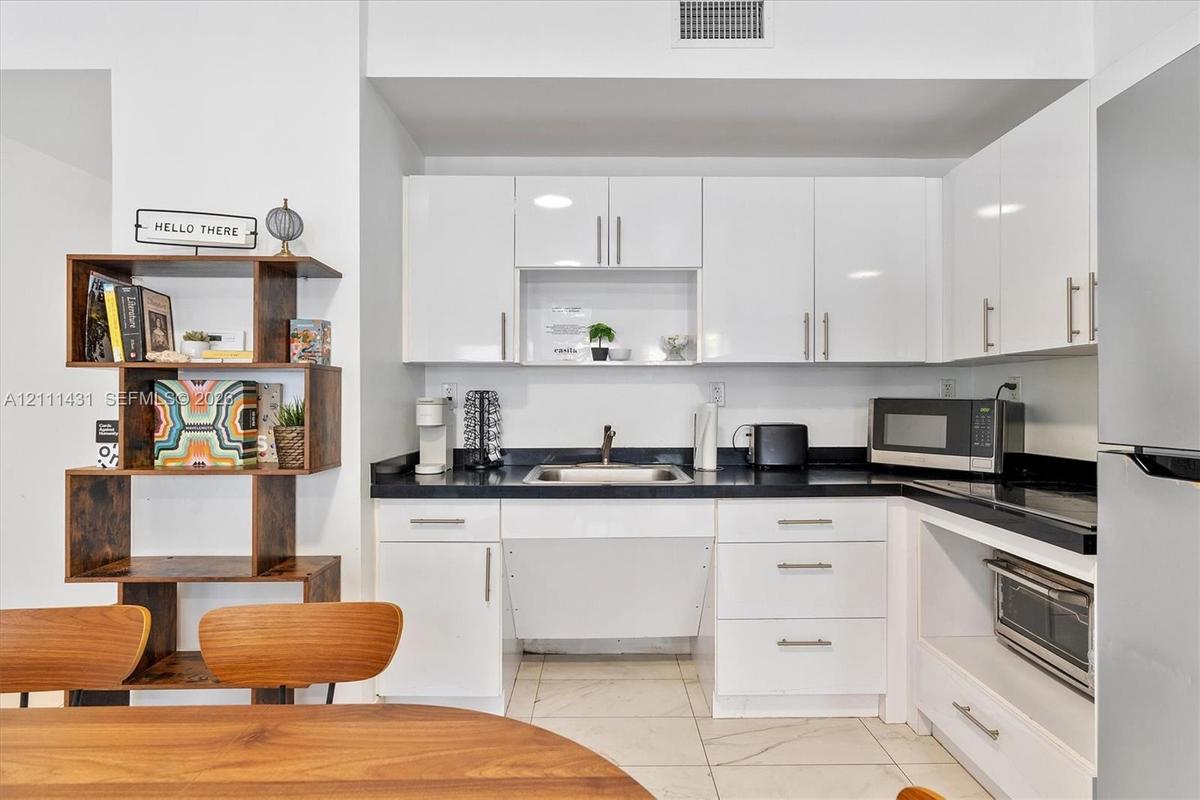 Kitchen featuring white high-gloss cabinetry, dark countertops, integrated stainless steel microwave, and tiled flooring