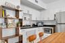 Kitchen featuring white cabinetry, contrasting dark stone countertops, stainless steel refrigerator, undermount sink with a gooseneck faucet, and ligh