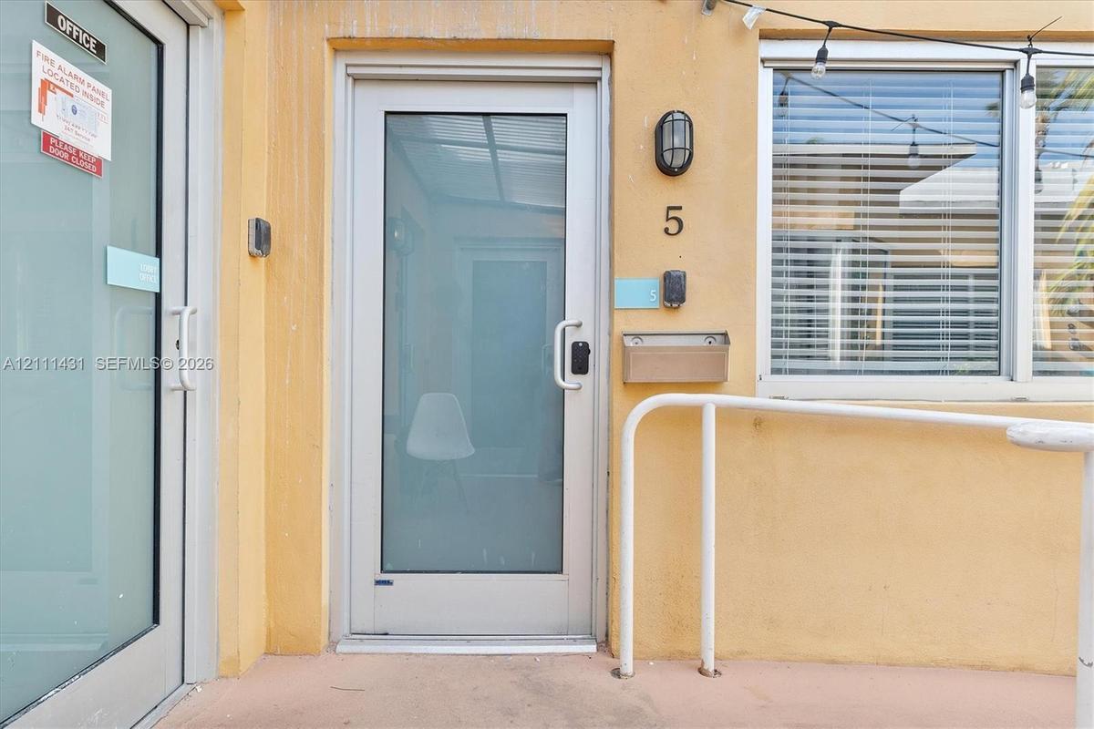 Full-glass entry door with metallic frame, wall-mounted exterior sconce, brushed metal mailbox, and aluminum handrail