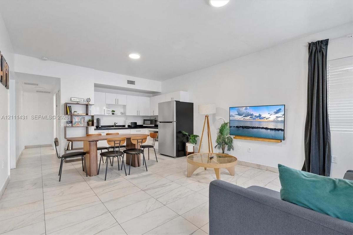 Open-concept floor plan featuring light-toned tile flooring, white cabinetry, dark countertops, and recessed lighting