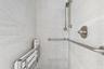 Shower enclosure featuring light grey stone-finish wall tiling, brushed nickel hardware, a wall-mounted shower head on a slide bar, and a fold-down wa