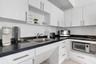 Kitchen featuring white flat-panel cabinetry, dark stone countertops, stainless steel sink with a high-arch faucet, and integrated appliance storage