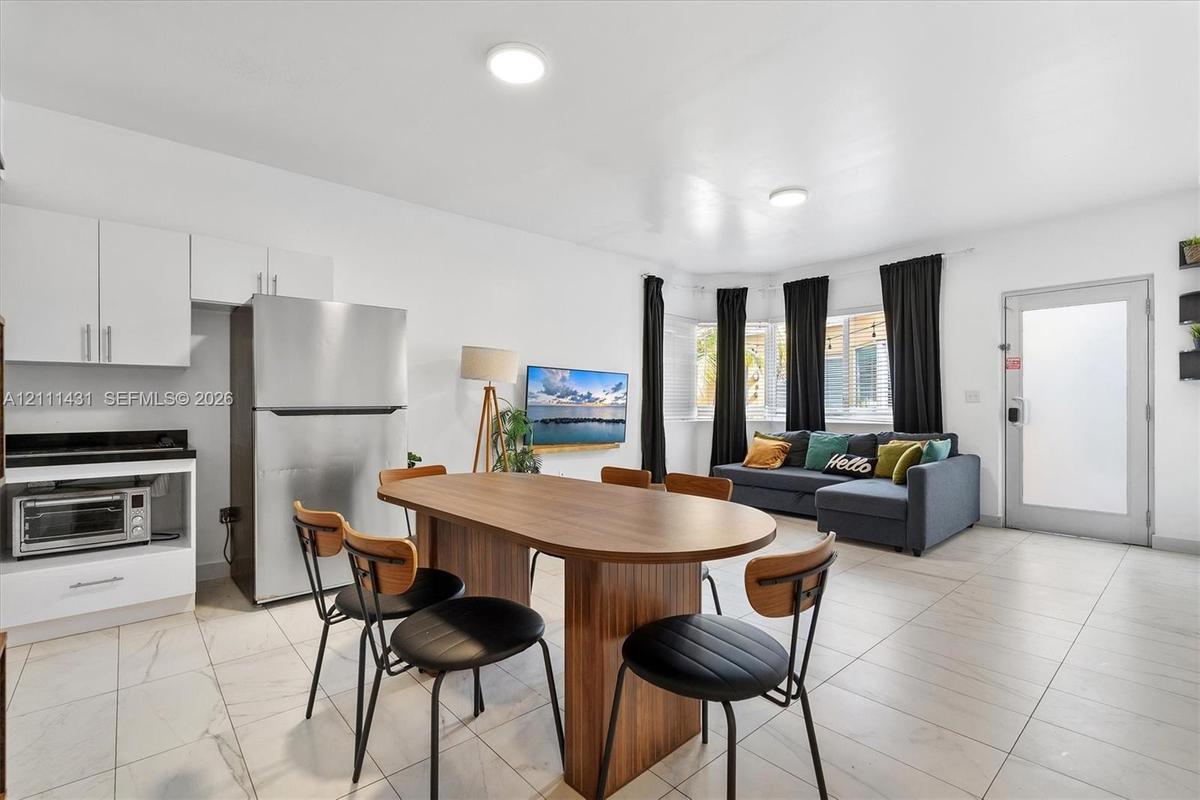 Open-concept kitchen area featuring white cabinetry, stainless steel refrigerator, stone-style countertops, light-toned tiled flooring, and a large ba