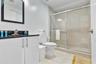 Bathroom featuring a vanity with dark stone countertop, rectangular undermount sink, walk-in shower with sliding glass doors, neutral tile wall surrou