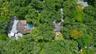 Aerial perspective of a multi-structure property featuring a screened-in swimming pool, shingled roofing, mature tree canopy, and paved driveway