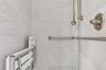Shower stall featuring floor-to-ceiling light-toned stone tile, brushed nickel wall-mounted shower head, handheld sprayer, and integrated support bars