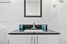 Vanity featuring a dark stone countertop, integrated rectangular sink, polished metal faucet, and white slab-style cabinetry with vertical pulls, topp