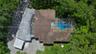 Aerial perspective featuring a multi-level roofline, screened-in swimming pool enclosure, detached covered parking structure, and mature trees on a wo